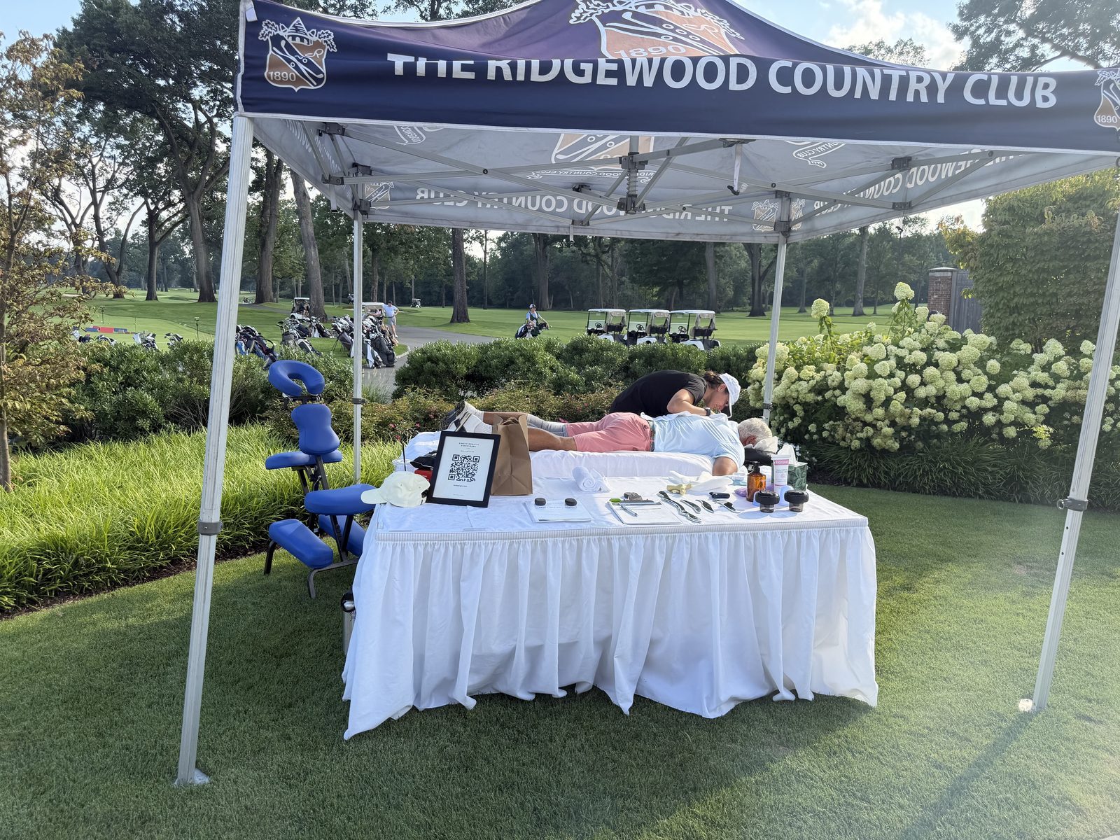 A Kinetic session underway under the tent at the Ridgewood Country Club, table set with tools and the booking QR, golf course beyond.